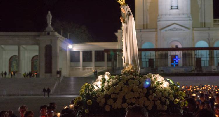 Procesión nocturna con velas llevando la estatua de Nuestra Señora de Fátima frente a la basílica.