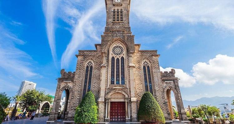 Stone Neo-Gothic Nha Trang Cathedral rising against a vivid blue sky with wispy white clouds.