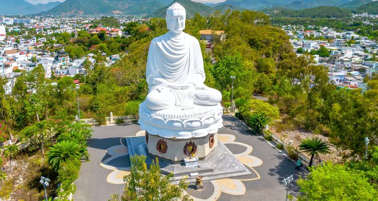 Giant seated white Buddha statue overlooking the city from a hilltop surrounded by greenery.