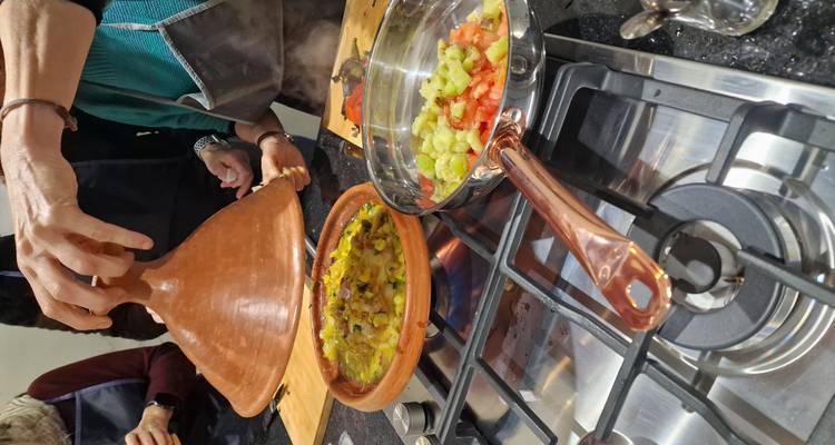 De instructeur tilt het deksel van een dampende tajine op en onthult kleurrijke groenten terwijl sautépannen in de buurt staan te koken.