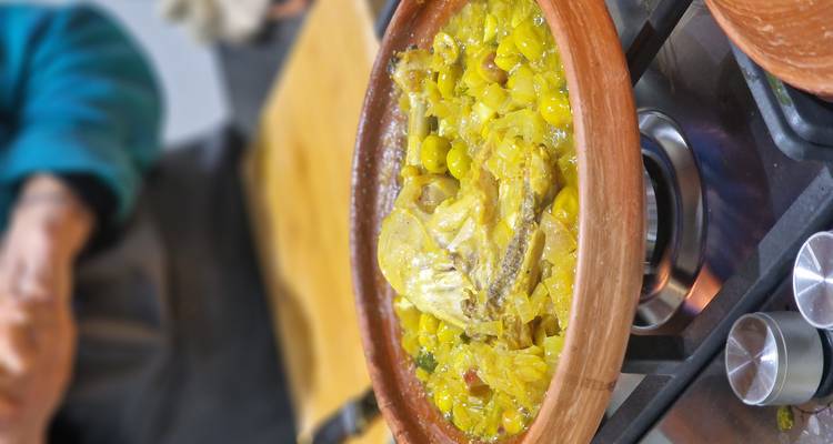 Close-up van een Marokkaanse tajine die pruttelt op een gasbrander, vol met gele groenten en kip.