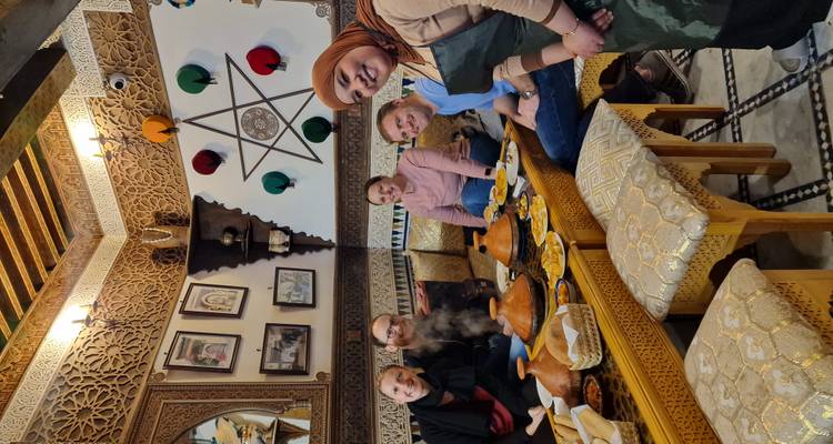 Glimlachende reizigers zitten rond een lage Marokkaanse tafel vol tajines en bijgerechten in een rijkelijk versierde riad.