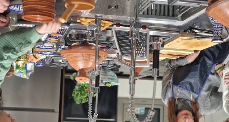 Deelnemers verzamelen zich rond moderne fornuizen, bereiden tajines voor en hacken ingrediënten fijn tijdens een kookworkshop.