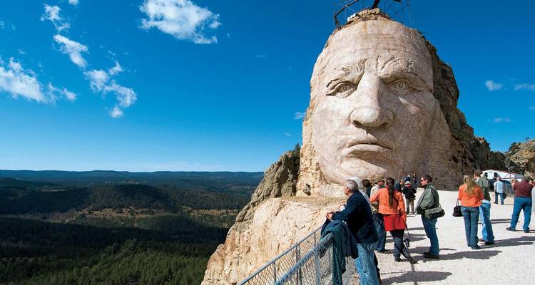 Los turistas ven la enorme cara de Caballo Loco tallada emergiendo de una montaña bajo un cielo despejado