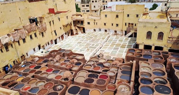 Vogelperspektive auf Gerbereibecken in Fes, gefüllt mit mehrfarbigen Farbstoffen, umgeben von sandsteinfarbenen Gebäuden.