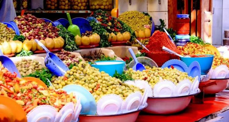 Lebendiger Marktstand, hoch aufgestapelt mit Schüsseln voller Oliven, Eingelegtem und Gewürzen in satten Rot-, Grün- und Gelbtönen.