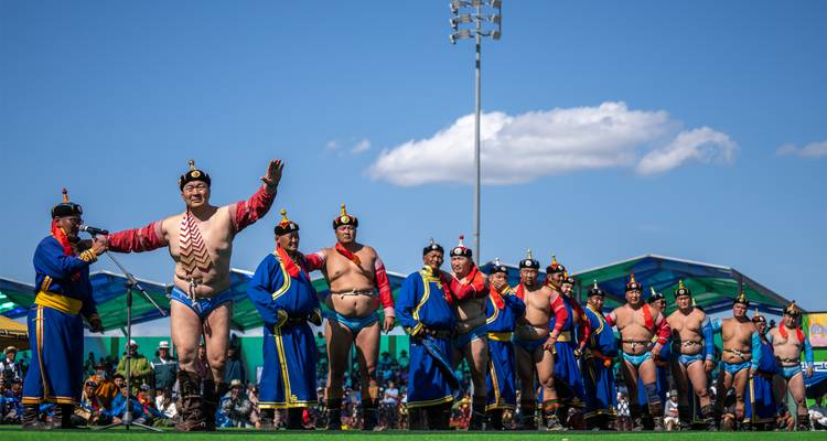 Row of Mongolian wrestlers in traditional costumes saluting the audience at a Naadam festival
