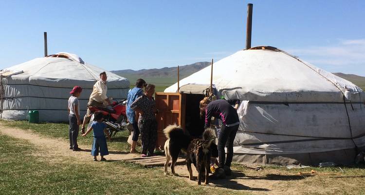 Local Mongolian family and visitors gathered near two gers with a dog and motorcycle outside