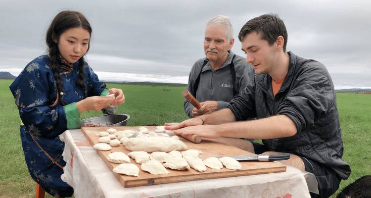 Travelers and local woman preparing dough and dumplings on a wooden board in an open field