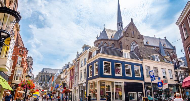 A lively Dutch shopping street lined with gabled houses and a tall church spire under a bright blue sky.