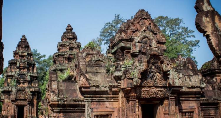 Les tours en grès rouge finement sculptées d'un ancien complexe de temples d'Angkor sous des cieux dégagés.