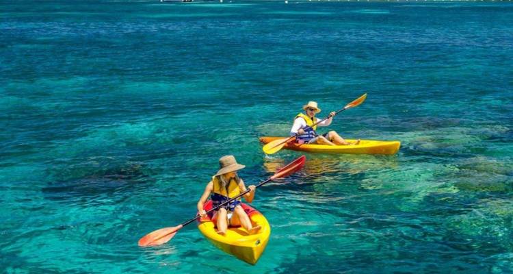 Deux kayakistes pagayant au-dessus d'une mer turquoise cristalline au-dessus d'un récif corallien.