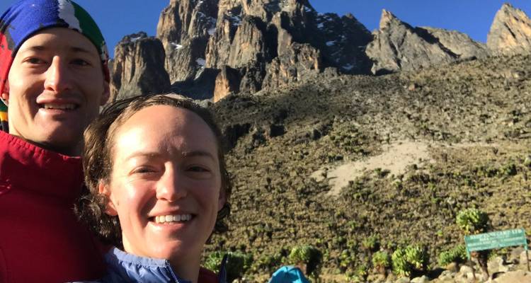 Smiling couple taking a selfie with the rocky summit of Mount Kenya in bright morning light behind them