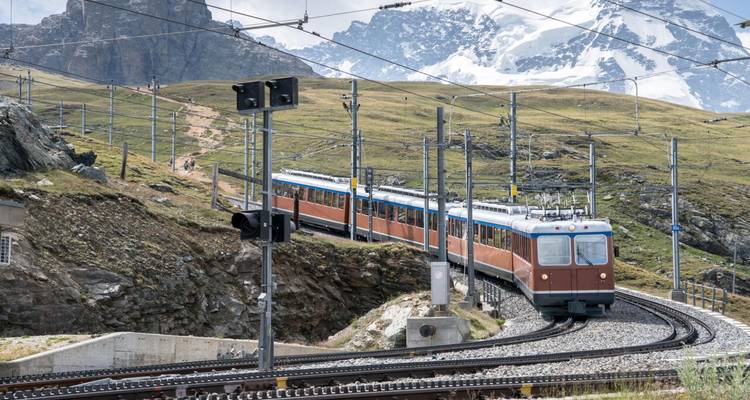 Tandradtrein die langs alpiene sporen kronkelt met ruige pieken en gletsjers op de achtergrond.