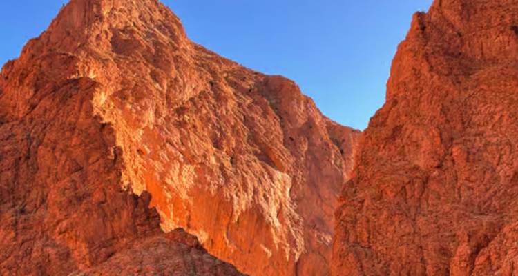 Torenhoge oranje canyonwanden gloeien tegen een diepe blauwe hemel in een smalle kloof.