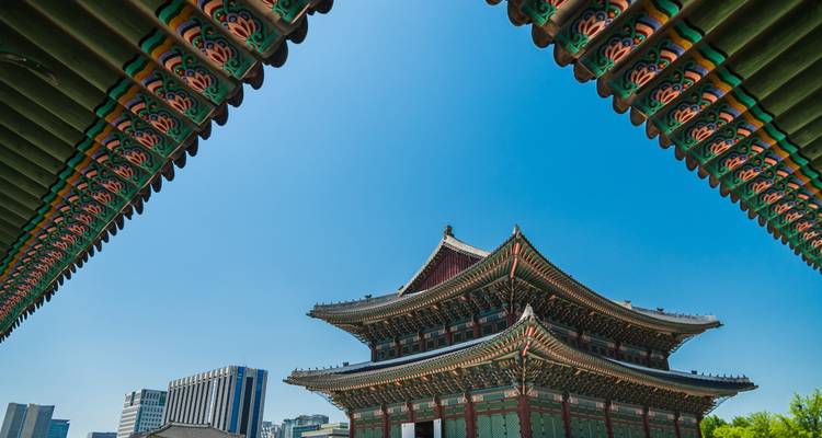 Ein traditionelles Palastdach und verzierte Dachtraufen rahmen einen klaren blauen Himmel über Seoul ein.