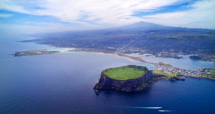 Luftaufnahme des Seongsan Ilchulbong Tuffkegels, der in die tiefblauen Gewässer vor der Insel Jeju ragt.