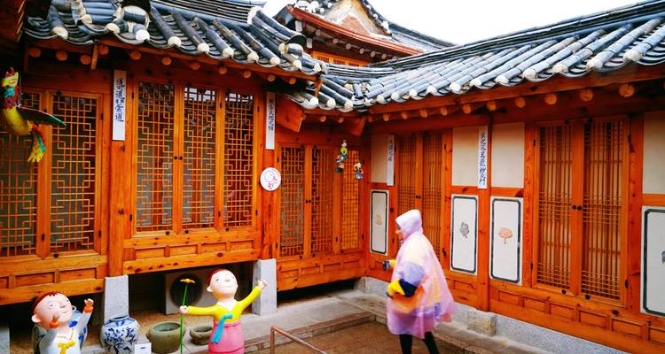 Ein Besucher in einem Regenponcho erkundet den Innenhof eines traditionellen Holz-Hanok.