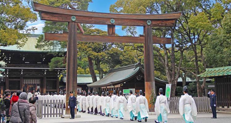 Sacerdotes sintoístas y visitantes pasando bajo la enorme puerta torii de madera del Santuario Meiji.
