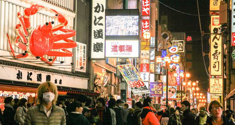 La bulliciosa calle Dotonbori iluminada por luces de neón por la noche con el famoso letrero gigante de cangrejo y multitudes de compradores y comensales.