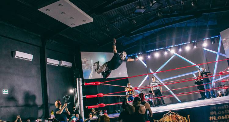 Le lutteur masqué s'élance des cordes dans une arène de lucha libre dramatique tandis que les fans et les arbitres regardent.