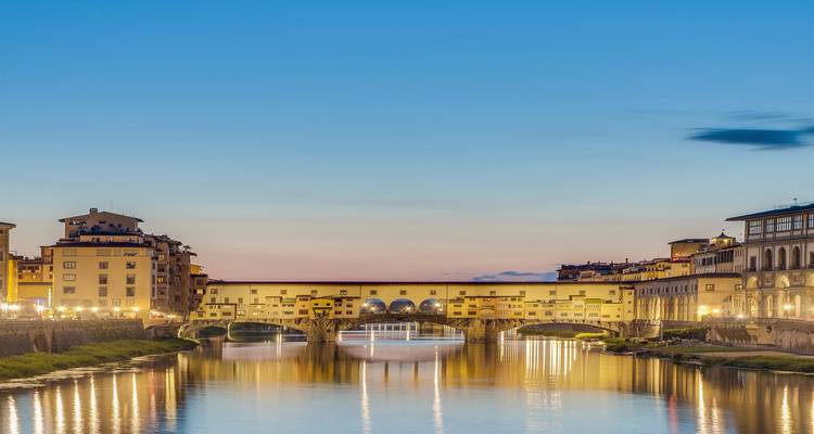 Sunset view over the Arno River with the illuminated Ponte Vecchio reflecting on the water in Florence.