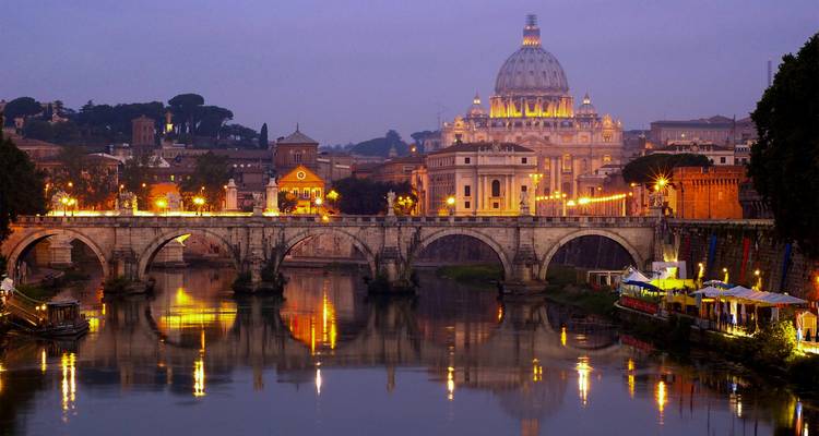 Twilight view of St Peter’s Basilica and the Tiber River with reflections of city lights in Rome.