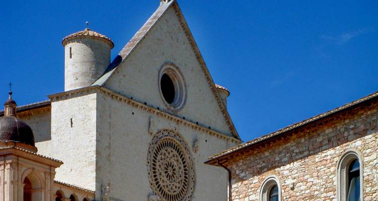 Stone façade and rose window of a historic basilica against a deep blue sky in Assisi.