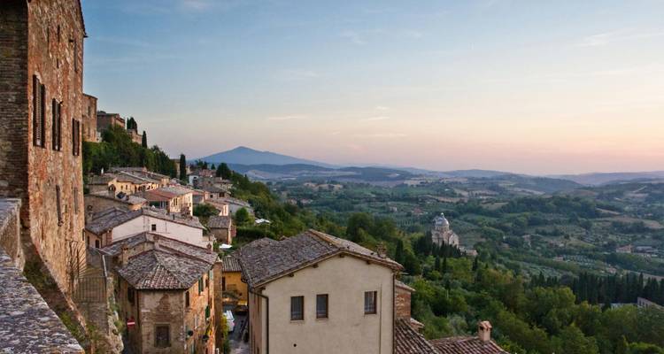 Panoramic view over rolling Tuscan hills and medieval stone houses at dusk near Montepulciano.