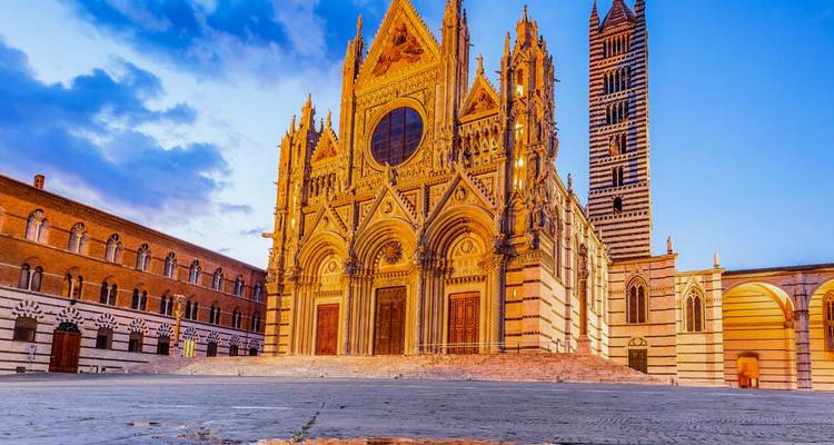 Dramatic sunrise light on the ornate façade of Siena Cathedral and its bell tower.