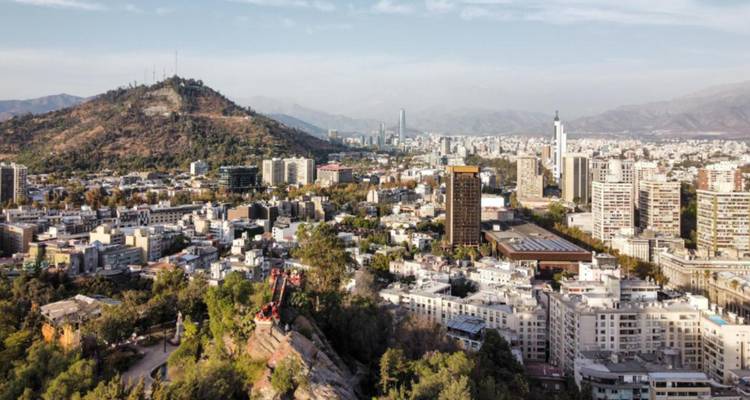 Wide cityscape of Santiago highlighting mixed modern and traditional buildings with a green hillside in the foreground.