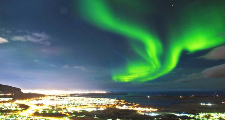Lebendige Nordlichter über einer nächtlichen Stadtlandschaft.