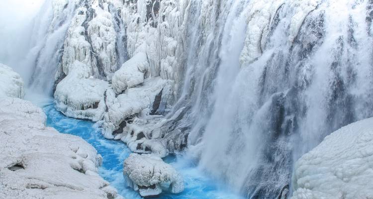 Krachtige ijzige waterval die in een helderblauw riviertje stort tussen sneeuwbedekte rotsen