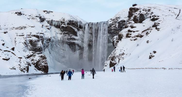 Toeristen lopen over een sneeuwwitte vlakte naar de imposante Skogafoss waterval in de winter