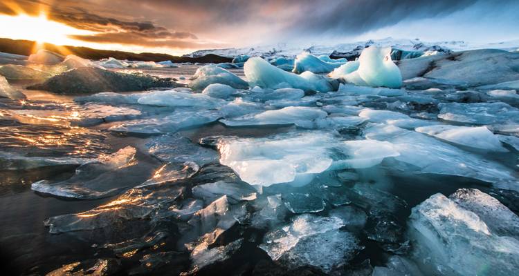 Zonsopgangsicht over gebroken blauwe ijsbergen die drijven in een gletsjermeer