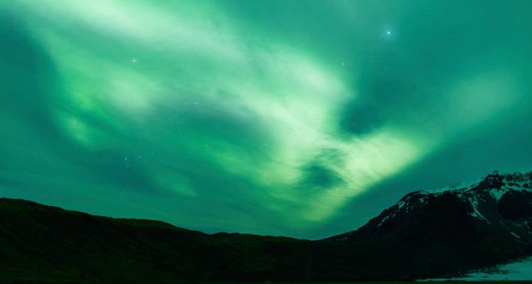 Aurora Borealis beleuchtet den Nachthimmel über den Bergen.