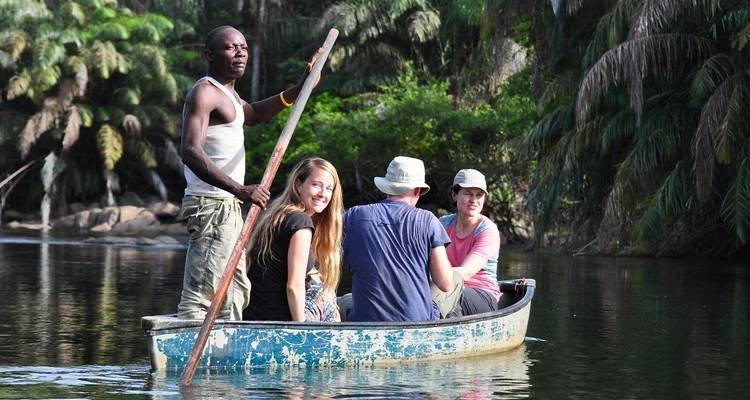 Small group paddling a weathered blue canoe through a lush tropical river lined with palms.