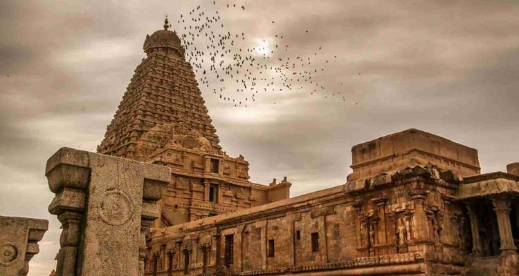 Un ciel nuageux spectaculaire surplombe la tour du temple Brihadeeswarar, construite en pierre, avec un vol d'oiseaux tournoyant au-dessus du sommet.