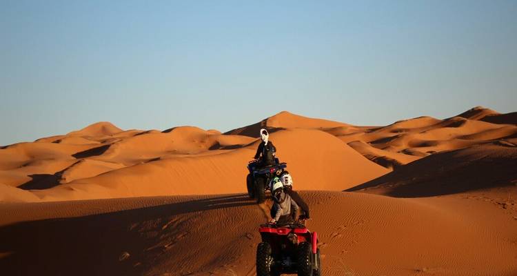 Les voyageurs chevauchent des quads sur les dunes ondulantes orange à la lumière de fin d'après-midi.