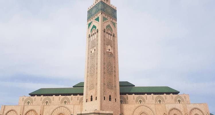Vue de face du minaret de la Mosquée Hassan II sur un ciel pâle.