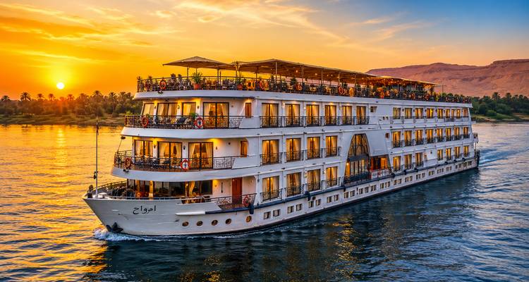Elegant Nile cruise ship sails at sunset with golden reflections on the river.