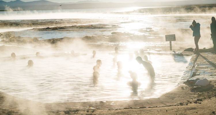 Les voyageurs se relaxant dans des sources chaudes fumantes au lever du soleil sur l'Altiplano