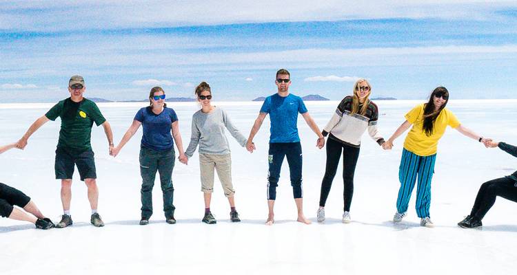 Groupe de voyageurs se tenant par la main sur le magnifique Salar de Uyuni blanc et scintillant sous un ciel bleu