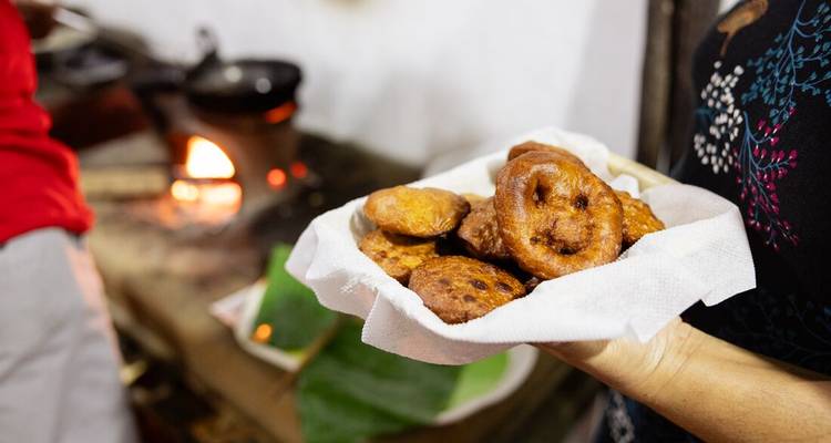 Plate of freshly fried Sri Lankan sweet fritters held on a napkin near a clay stove fire.