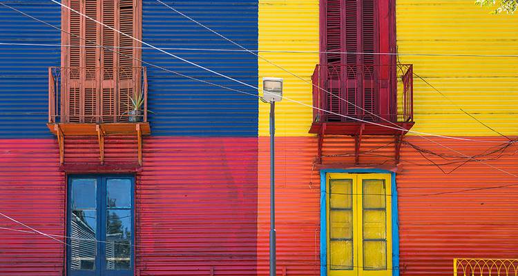 Brightly painted corrugated metal façade divided into bold blocks of blue, red, yellow and orange with shuttered balconies.