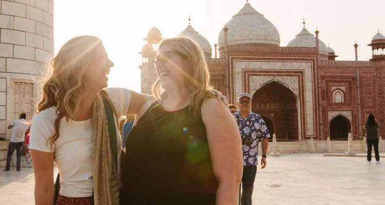 Two friends laugh together in the marble courtyard beside the Taj Mahal mosque at sunset.