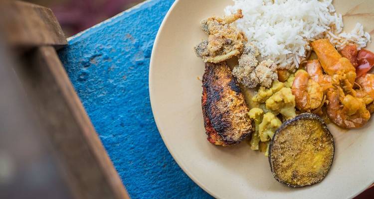 Plated Indian meal with rice, prawns and grilled fish set against a bright blue tabletop.