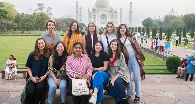 Tour group poses happily on a bench with the Taj Mahal towering behind.