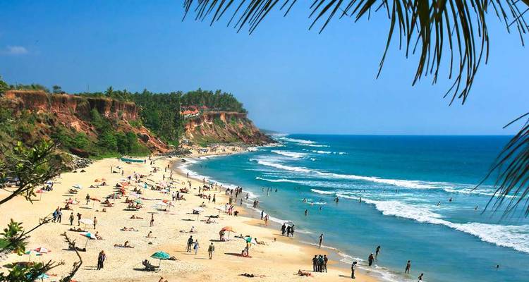 Cliff-backed Varkala beach with sunbathers and rolling waves under a bright blue sky.