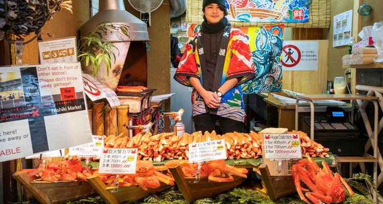 Un vendeur de marché se tient derrière des présentoirs vibrants de pattes de crabe frais et de panneaux de prix manuscrits.